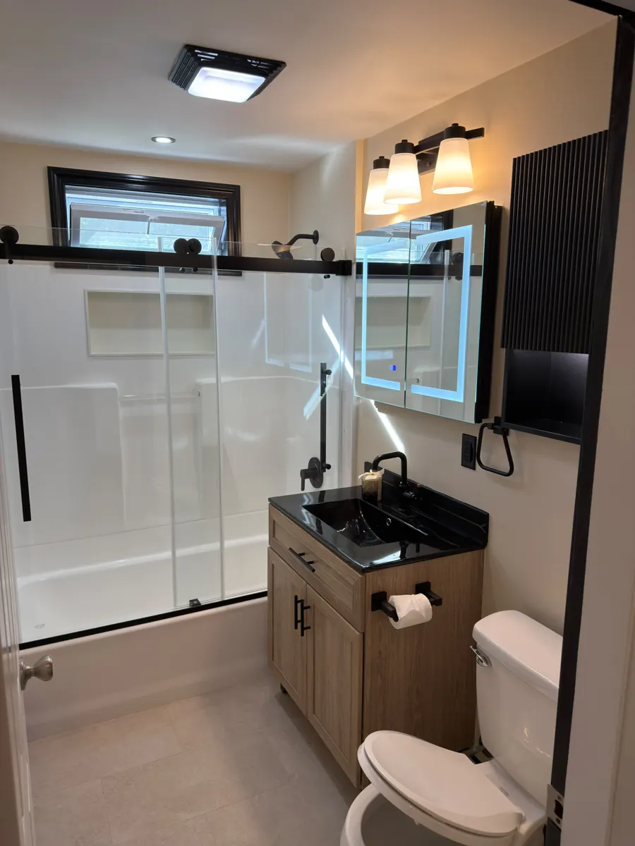 Remodeled bathroom with sliding glass shower door, black fixtures and wood vanity
